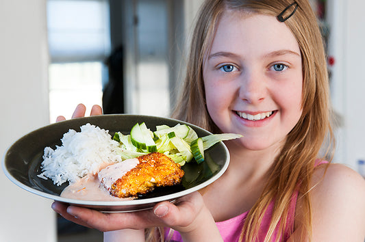 Flicka håller tallrik med panerade torskslag, ris, sås och sallad – Isfisk
